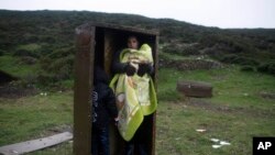 ស្រ្តី​ជនជាតិ​ស៊ីរី​ម្នាក់​ជាមួយ​នឹង​កូន​របស់​គាត់​យក​ប្រអប់​ដែក​មួយ​ធ្វើ​ជា​ជម្រក​ក្នុង​ពេល​ភ្លៀង បន្ទាប់​ពី​ទៅ​ដល់​កោះ Pasas របស់​ក្រិក​ កាលពី​ថ្ងៃទី២០ ខែមករា ឆ្នាំ២០១៦។