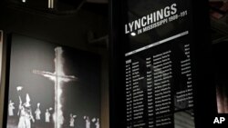 FILE - A monolith listing the names, dates and rationale for the lynching of African-American residents rests in the foreground of a photograph of a burning Ku Klux Klan cross on display in the Mississippi Civil Rights Museum in Jackson, Miss., Nov. 10, 2017. The facility is adjacent to the new Museum of Mississippi History that documents the state's rich history and the diversity of its people. 