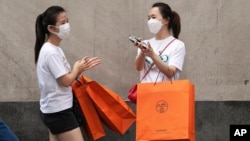 Women carrying Hermes shopping bags use hand sanitizer as they walk on Wall Street, July 30, 2020, in New York.