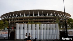 Pejalan kaki yang menggunakan masker pelindung, pasca wabah COVID-19, berjalan di depan Stadion Nasional, stadion utama Olimpiade dan Paralimpiade Tokyo 2020 di Tokyo, Jepang, 7 Juli 2021. (Foto: Reuters)