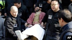 FILE - Kim Ki-jong, the suspect of slashing U.S. Ambassador Mark Lippert, in a wheelchair is carried by police officers as he leaves a police station for Seoul Central District Court in Seoul, South Korea, March 6, 2015.