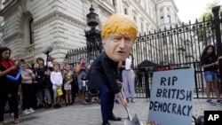 man in a giant Boris Johnson 'head' digs a grave at the foot of a pretend tombstone outside Downing Street in London, Wednesday, Aug. 28, 2019. 