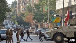 Para pejuang kelompok Hezbollah tampak berjalan melewati tentara Lebanon di area bentrokan yang terjadi di kota Beirut pada 14 Oktober 2021. Bentrokan tersebut telah menewaskan tujuh orang. (Foto: AFP/Anwar Amro)