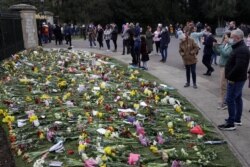 People look at flowers outside Windsor Castle in Windsor, England, to pay tribute to Britain's Prince Philip, the irascible and tough-minded husband of Queen Elizabeth II.