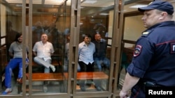 Defendants in the murder trial of Russian investigative journalist Anna Politkovskaya are seen inside a glass-walled cage, with a policeman standing guard in the foreground, during a court hearing in Moscow, June 9, 2014.