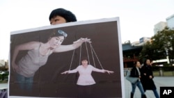 Seorang mahasiswa Korea Selatan membawa plakat bergambar Presiden Park Geun-hye (kanan bawah) sebagai boneka 'marionette' dan Choi Soon-sil (tengah) sebagai dalang dalam sebuah aksi demo di Seoul, Korea Selatan, 3 November 2016 (Foto: dok). Choi Soon-sil, menolak untuk hadir di hadapan komisi Majelis Nasional, Rabu (7/12).