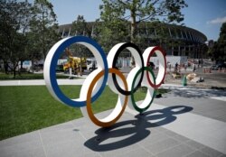 FILE - Construction workers and passersby are seen through Olympic rings in front of the construction site of the New National Stadium, the main stadium of Tokyo 2020 Olympics and Paralympics, in Tokyo, Japan, June 13, 2019.