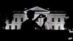 FILE - A tourist takes a photo from Pennsylvania Avenue of an illuminated White House in Washington, Aug. 25, 2017. 