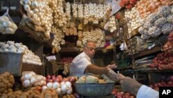 A vendor exchanges money with a customer at a shop selling garlic, onions and potatoes at a wholesale market in Mumbai, April 28, 2011.