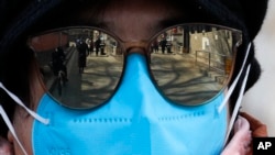 People are reflected on a volunteer's sunglasses outside a closed neighborhood alley following the coronavirus outbreak in Beijing, Sunday, March 1, 2020. (AP Photo/Andy Wong)