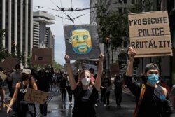 A woman holds a sign showing George Floyd, who died after being restrained by Minneapolis police, while marching on Market Street at a protest calling for an end to racial injustice and accountability for police in San Francisco, June 20, 2020.