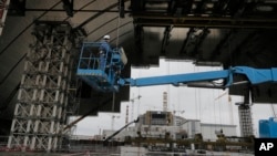 FILE - Construction workers assist in the assembly of a gigantic steel arch to cover the remnants of the exploded reactor at the Chernobyl nuclear power plant in Chernobyl, Ukraine, March 23, 2016.