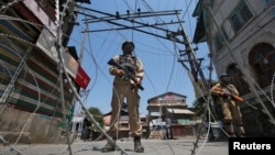 Indian policemen stand guard behind concertina wire during a strike called by separatists to mark the death anniversaries of chief cleric of Kashmir, Moulana Mohammad Farooq and Abdul Gani Lone, a Kashmiri separatist leader, in Srinagar, May 21, 2018.