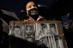 FILE - A demonstrator carries a sign bearing images of former Minneapolis police Officer Derek Chauvin and others, during a protest April 15, 2021, in Brooklyn Center, Minn.