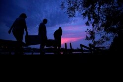People carry supplies to their boat at dusk in the aftermath of Hurricane Ida, Sept. 1, 2021, in Jean Lafitte, La.