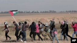 Palestinian masked protesters carrying tires walk toward the border fence during clashes with Israeli troops along Gaza's border with Israel, east of Khan Younis, Gaza Strip, April 5, 2018. 