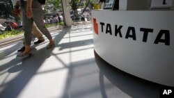 FILE - Visitors walk by a Takata Corp. desk at an automaker's showroom in Tokyo.