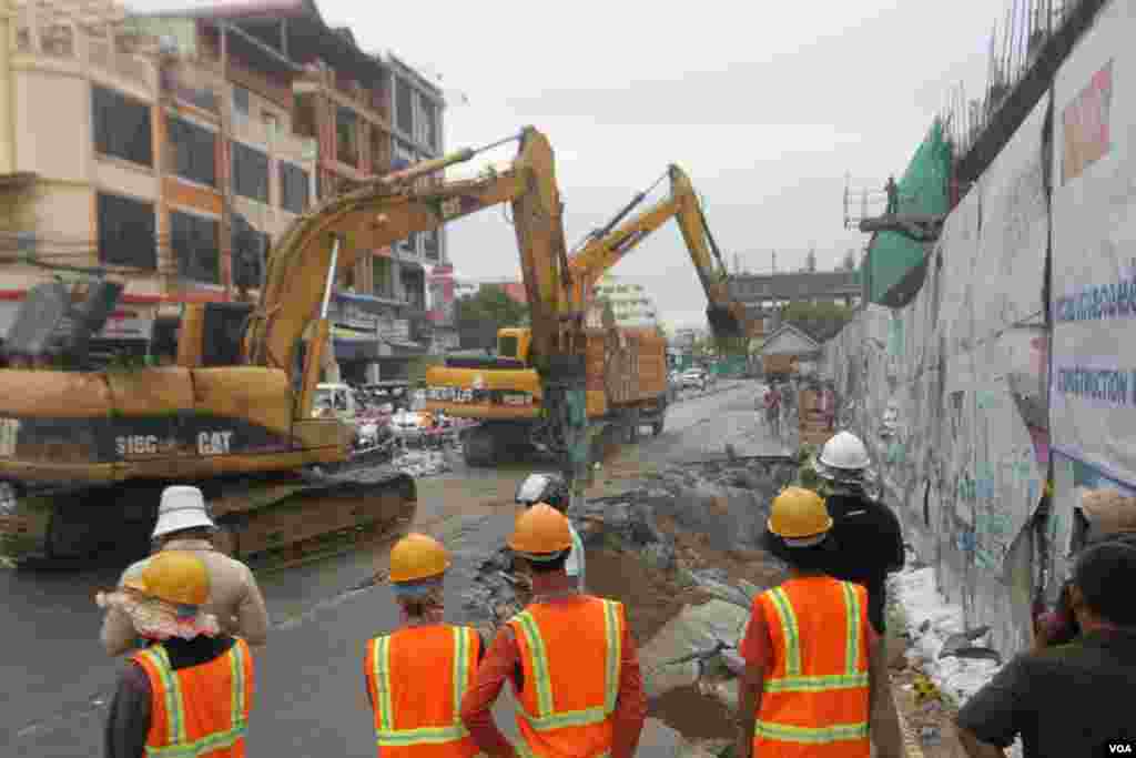 កម្មករ​សំណង់​ឈរ​មើលរថ​យន្ត​អេស្កា​វាទ័រ​ជីក​កកាយ​ដី ​បន្ទាប់​ពី​រថយន្ត​បី​គ្រឿង​ផុង​ស្រុត​ ខណៈពេល​មាន​ភ្លៀង​ធ្លាក់​ជោគជាំ​​នៅ​ការដ្ឋាន​​សំណង់​​នៅ​ជាប់​របង​ពហុកីឡា​ដ្ឋានជិត​​អូឡាំពិក​ ខណ្ឌ​ប្រាំពីរ​មករា ​នៅ​ថ្ងៃ​ពុធ​ ទី​០៧​ខែ ​មិថុនា​ ឆ្នាំ​២០១៦​នេះ​។​ រថយន្ត​ចំនួន​បី​គ្រឿង​ដែល​គេ​ចត​ចោល​នៅបណ្ដោយ​ផ្លូវ​ជាប់​ការរដ្ឋាន​នេះ ត្រូវ​ក្រុម​ហ៊ុន​ការដ្ឋាន​សាងសង់​ស្ទួច​ទៅ​ឲ្យ​ម្ចាស់​ដើម​វិញ​។ ​(ឡេង ឡែន/VOA )