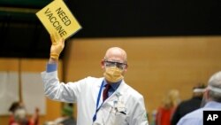 វេជ្ជបណ្ឌិត John Corman នៃ​មជ្ឈមណ្ឌល​សុខភាព Virginia Mason Franciscan Health លើក​ស្លាកសញ្ញា​មួយ​ដែល​សរសេរ​ថា «ត្រូវការ​វ៉ាក់សាំង» ដើម្បី​ជា​សញ្ញាប្រាប់​ឲ្យ​បុគ្គលិក​យក​វ៉ាក់សាំង Pfizer សម្រាប់​បង្ការ​ជំងឺ​កូវីដ១៩ ឲ្យ​លោក​បន្ថែម​ទៀត ថ្ងៃ​ទី២៤ ខែមករា ឆ្នាំ២០២១។ 