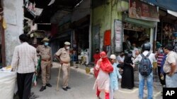 Policemen stand guard as people shop during a limited opening of small grocery stores amid the coronavirus pandemic, in Prayagraj, India, April 25, 2020.