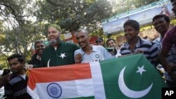 Mohammad Bashir (ketiga dari kiri), penggemar kriket dari Pakistan dan Sudhir Kumar (keempat dari kanan), warga India, membentangkan bendera India dan Pakistani yang dijahit jadi satu di depan stadion Chinnaswamy di Bangalore, India (25/12).