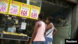 FILE - Women look at prices at a food market in Rio de Janeiro, Brazil, Jan. 21, 2016.