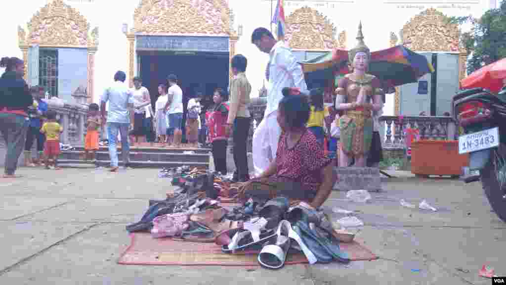 ស្រ្តី​ម្នាក់​អង្គុយ​យាម​ស្បែកជើង​របស់​ពុទ្ធសាសនិក​ នៅ​វត្ត​សុវណ្ណគីរីរតនៈភ្នំប្រុស (ហៅ​វត្ត​ភ្នំប្រុស) ក្នុង​ស្រុក​កំពង់សៀម ខេត្ត​កំពង់ចាម នៅ​ថ្ងៃ​ភ្ជុំបិណ្ឌ កាលពី​ថ្ងៃទី០១ ខែតុលា ឆ្នាំ២០១៦។ (ប៊ុន ប៉េងហ៊ុយ/VOA)