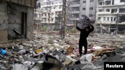 A man carries a bag amid damage and debris in the besieged area of Homs, Jan. 26, 2014. 