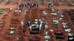 FILE - Cemetery workers wearing protective gear lower the coffin of a person who died from complications related to COVID-19 into a gravesite at the Vila Formosa cemetery in Sao Paulo, Brazil, April 7, 2021.