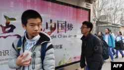 2018年3月12日，北京一所学校外面，青少年走过宣传牌，牌上写着中英文口号“点亮中国梦 知识改变命运 付出收获财富”。