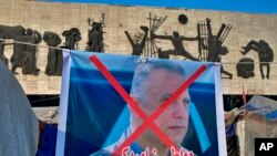 A poster with a defaced picture of Mustafa Kadhimi, Iraq's intelligence chief and new prime minister-designate, is shown in Tahrir Square, Baghdad, Iraq, Saturday, April 11, 2020. 