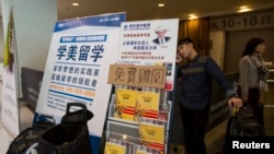 Seorang mahasiswa China berbicara di telepon di belakang poster iklan pendidikan luar negeri usai tes SAT (Scholastic Assessment Test) di AsiaWorld-Expo, Hong Kong, 2 November 2013. (Foto: Reuters)