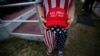 FILE - A man dressed in American flag clothes holds "Make America Great Again" hats at a December 2016 rally in Mobile, Alabama.