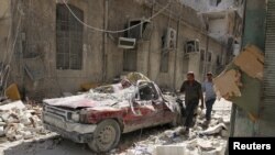 People walk near a damaged vehicle after an airstrike Sunday in the rebel-held besieged al-Qaterji neighborhood of Aleppo, Syria, Oct. 17, 2016. 