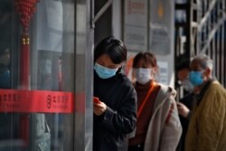 People wait in a queue to get temperature check before entering a bank in Beijing, March 11, 2020.