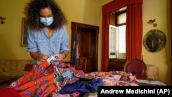 Fashion designer Stella Jean wears a face mask to stop the spread of COVID-19 as she holds fabrics during an interview with the Associated Press, in Rome, on Wednesday, February 24, 2020. (AP Photo/Andrew Medichini)