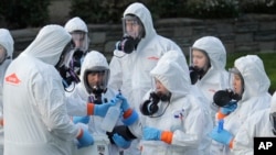 Workers from a Servpro disaster recovery team wearing protective suits and respirators are given supplies as they line up before entering the Life Care Center in Kirkland, Wash., to begin cleaning and disinfecting the facility, Wednesday, March 11, 2020…