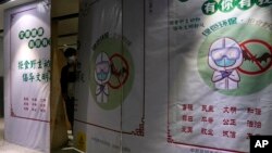 FILE - A worker wearing a mask peeps out behind construction barrier with a notice depicting a bat and advocating for people not to eat wild animals at the airport in Kunming in southern China's Yunnan province on Thursday, Dec. 3, 2020. (AP Photo/Ng Han Guan)