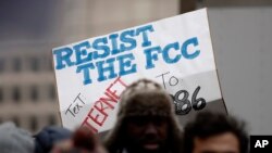 FILE - A protester holds a sign that reads "Resist the FCC. Text: INTERNET To: 52886" at the Federal Communications Commission in Washington, Dec. 14, 2017. 