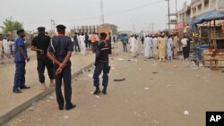 Security officers stand guard at the scene of an explosion at a mobile phone market in Kano, Nigeria. Wednesday Nov. 18, 2015. 
