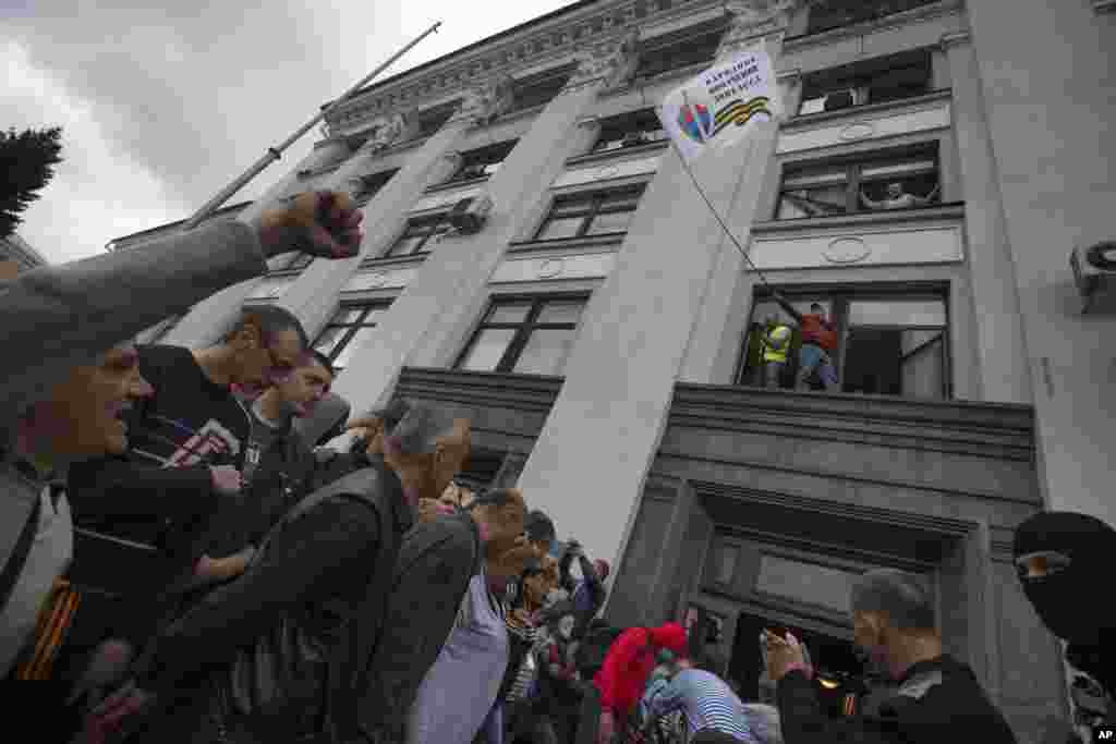 A Pro-Russian activist waves a Donbas Republic flag over a crowd celebrating the capture of an administration building in the center of Luhansk, Ukraine, April 29, 2014.