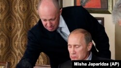 RUSSIA – Evgeny Prigozhin (L) assists Russian Prime Minister Vladimir Putin during a dinner with foreign scholars and journalists at the restaurant Cheval Blanc on the premises of an equestrian complex outside Moscow, November 11, 2011