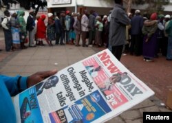 A man reads a newspaper as residents line up to draw money at a bank in Harare, Zimbabwe, Nov. 17, 2017.