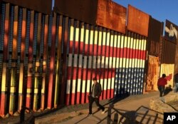 People pass graffiti along the border structure in Tijuana, Mexico, Jan. 25, 2017.