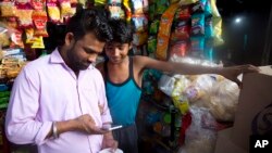 In this Monday, April 8, 2019, photo, a customer watches election campaign advertisements on his mobile phone outside a shop in New Delhi, India. (AP Photo/Manish Swarup)