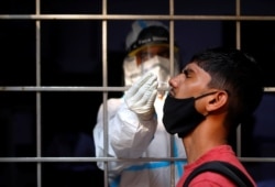 A man reacts as a health care worker collects a swab sample to test for the coronavirus, at a testing site, in New Delhi, India, Oct. 17, 2020.