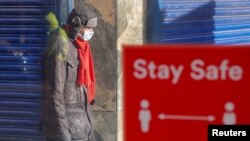 A person wearing a protective mask walks near a social-distancing sign, amid the outbreak of the coronavirus disease, in Coventry, Britain, Oct. 25, 2020. 