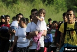 A man carries a child along with other Hondurans fleeing poverty and violence and heading toward the United States, in San Pedro Sula, Honduras, Oct. 13, 2018.