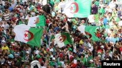 FILE - Demonstrators gesture and carry flags during a protest demanding the removal of the ruling elite and prosecution of former officials linked to former President Abdelaziz Bouteflika, in Algiers, Algeria, June 14, 2019.