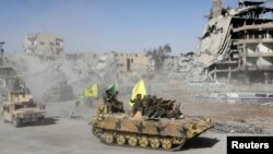 FILE - Syrian Democratic Forces (SDF) fighters ride atop of military vehicles as they celebrate victory in Raqqa, Syria, Oct. 17, 2017. 